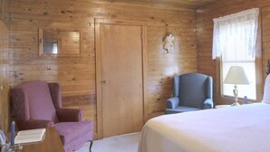 A wooden room with a bed, a chair, a desk, and a lamp.