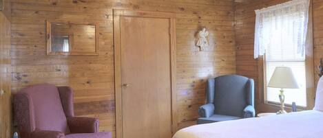 A wooden room with a bed, a chair, a desk, and a lamp.