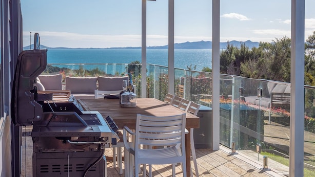A covered outdoor area with a grill, seating, and a view of the sea.