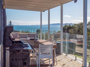 Et overdækket udendørs område med grill, siddepladser og havudsigt.