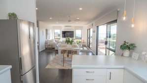 A modern kitchen with a stainless steel refrigerator, white cabinetry, and a dining area with a table and chairs.