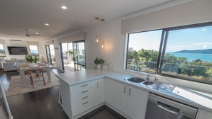 A modern kitchen with a large island, stainless steel appliances, and a view of the sea.