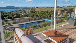 A balcony with a view of a swimming pool, a wooden deck, and a seating area with cushions.