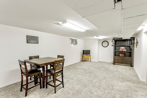 Un comedor con mesa y sillas de madera, un televisor sobre un soporte, un reloj en la pared y una estantería con adornos.