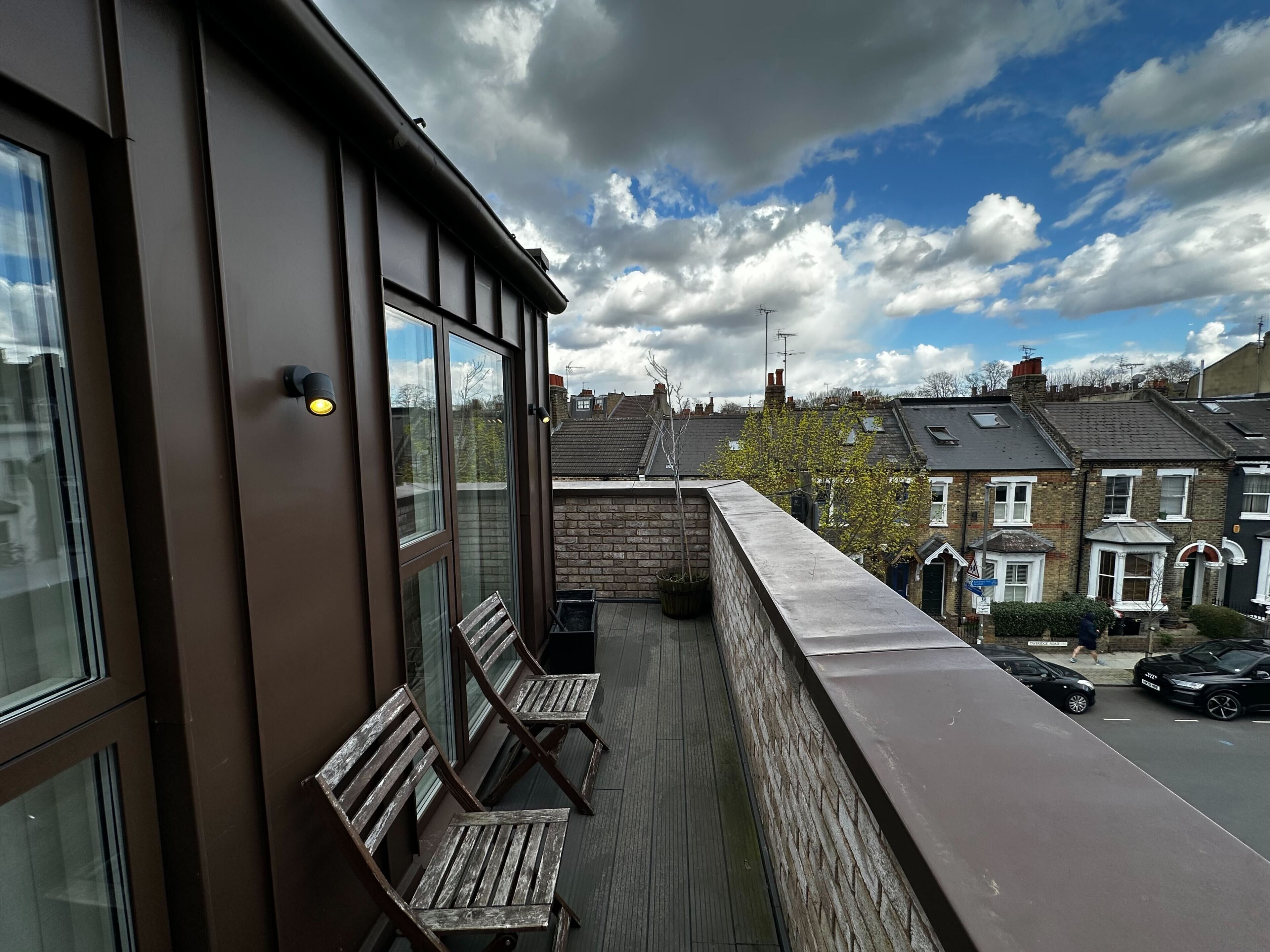 Ein Balkon mit Holzbanken, Blick auf eine Wohnstraße und ein teilweise bewölkter Himmel.