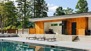 A modern house with a swimming pool, wooden exterior, and a patio with lounge chairs.