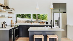 A modern kitchen with a large island, black cabinets, stainless steel appliances, and a view of the outdoors.