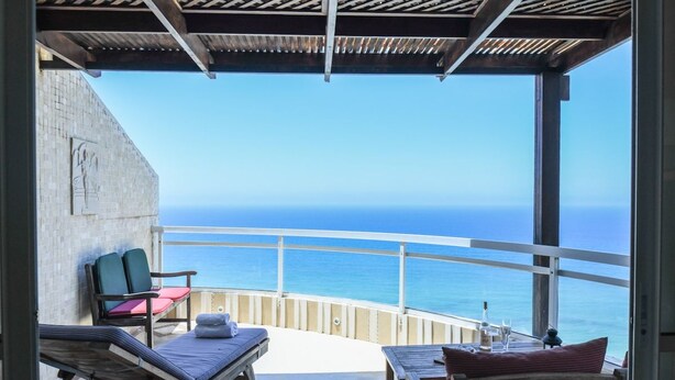 Un balcon avec vue sur la mer, une chaise longue, une petite table et une chaise.