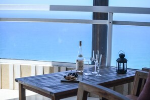 Un tavolo di legno con una bottiglia, bicchieri e una lanterna su un balcone affacciato sul mare.