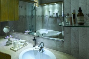 Ein Badezimmer mit Duschkabine aus Glas, einem großen Spiegel, einem weißen Waschbecken und einer Glasablage mit Pflegeprodukten.