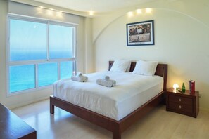 Una camera da letto con un'ampia finestra, un letto con lenzuola bianche, un comodino con libri e un quadro appeso al muro.