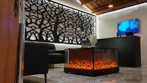 Un salón con chimenea, un sofá negro, un panel decorativo y un televisor de pantalla plana.