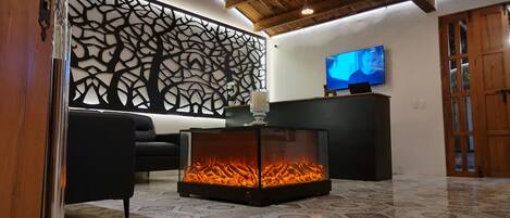 A living room with a fireplace, a black sofa, a decorative wall panel, and a flat-screen TV.