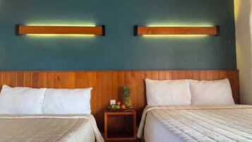 Habitació d'hotel amb dos llits, un capçal de llit de fusta, parets color cel i una petita taula de nit de fusta amb fruita.