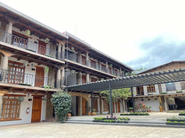 Un edificio de varios pisos con balcones, un patio cubierto y plantas en macetas.