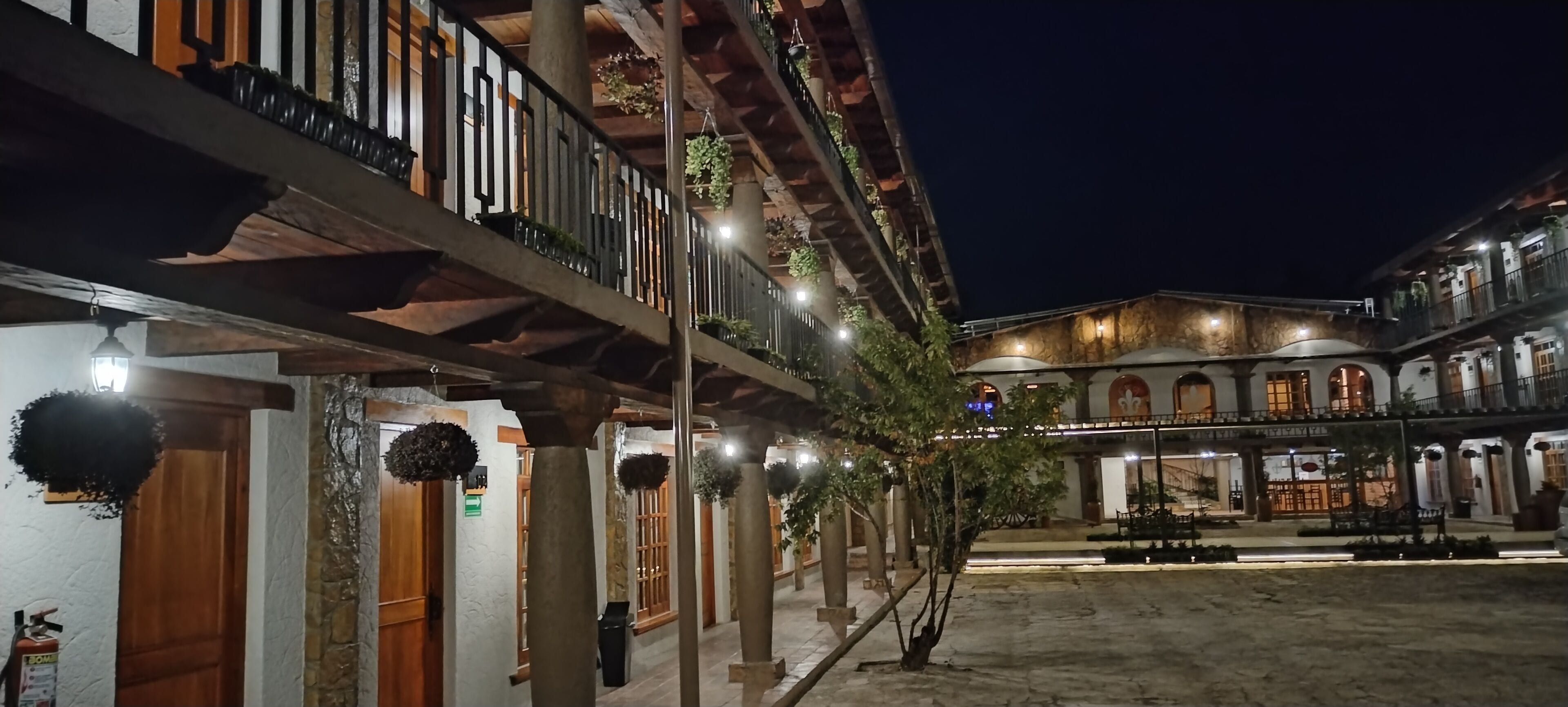 Un patio con balcón de madera, pilares de piedra y plantas colgantes.