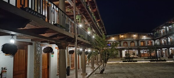 Un patio con balcón de madera, pilares de piedra y plantas colgantes.