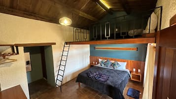 Un dormitorio pequeño y rústico con literas, una escalera, una mesita de noche y una cama con ropa de cama estampada.