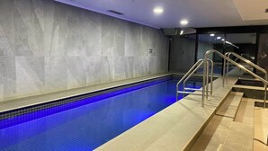 A swimming pool with blue tiles, a metal handrail, and a tiled floor. - Spacious CBD Penthouse w Parking Pool and Gym (West Melbourne)