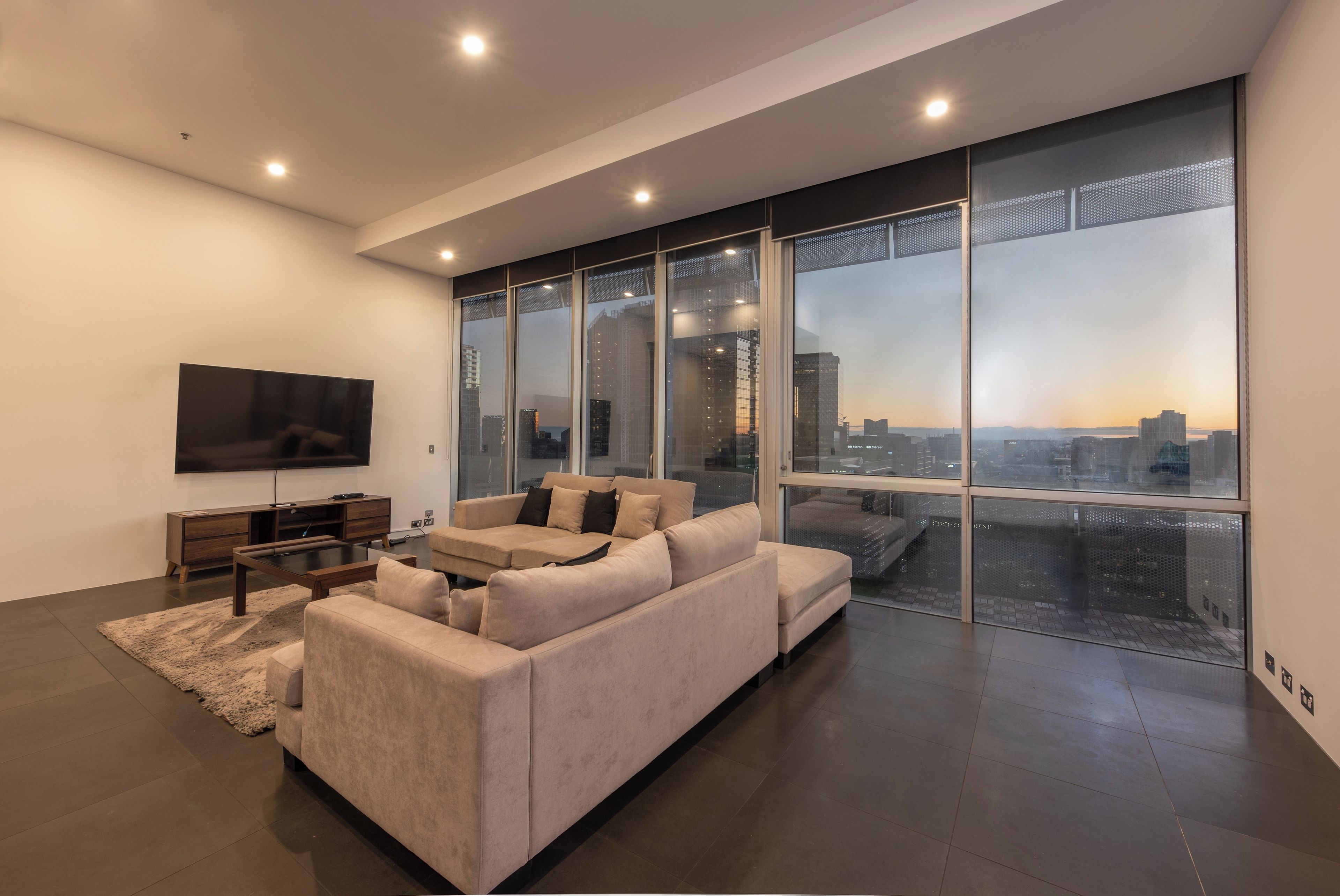 Una sala de estar moderna con un sofá modular grande, un televisor de pantalla plana y vistas a la ciudad a través de ventanales.