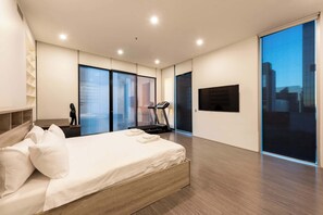 Quarto moderno com cama, equipamentos de ginástica e vista para a cidade.
