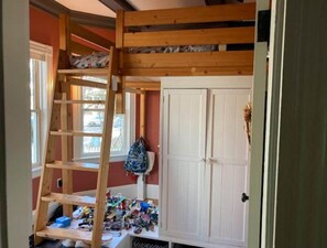 A room with a bunk bed, a ladder, a white wardrobe, and a window.