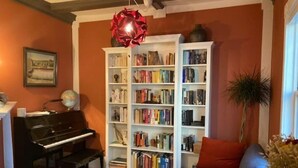 Ein Wohnzimmer mit einem Klavier, Bücherregalen, einem Sofa und einem Globus auf einem Tisch.