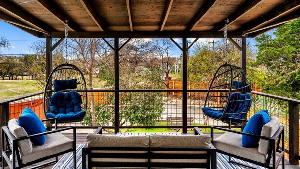 Et udendørs overdækket opholdsområde med to hængestole og en bænk, med udsigt over en anlagt have og et boligområde.