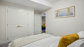 Une chambre à coucher avec un lit, des murs blancs et une porte. Il y a trois tableaux encadrés accrochés au mur.