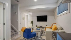 Un salon moderne avec un canapé, un fauteuil bleu et un téléviseur à écran plat fixé au mur.