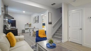 Un salon moderne avec un canapé, une table basse et un fauteuil bleu. Un escalier mène à un autre niveau.