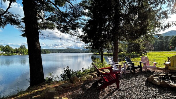 Un espace de détente aménagé au bord du lac, avec des fauteuils Adirondack et une petite table, entouré d’arbres et offrant une vue sur le lac.