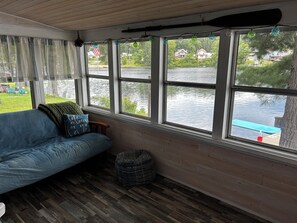 A room with a wooden floor, a blue sofa, and a view of a lake through large windows. - A cozy Adirondack cabin with mountain and lake views! (Wells)