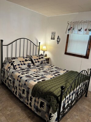 A bed with a checkered quilt, a bedside lamp, and a window with blinds. - A cozy Adirondack cabin with mountain and lake views! (Wells)