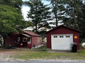 A rustic cabin with a red exterior, a white garage door, and a moose crossing sign. - A cozy Adirondack cabin with mountain and lake views! (Wells)
