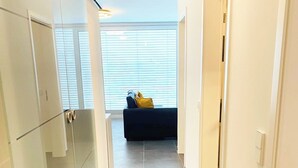 A narrow hallway with a dark tiled floor, white walls, and a blue sofa with yellow cushions in the background.