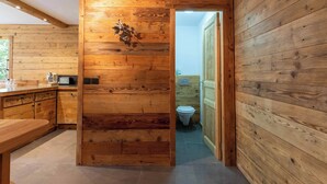 A wooden interior with a kitchen area, a wooden door leading to a bathroom, and a bench. - Fauvettes 4 a warm cocoon in Meribel Village (Les Allues)