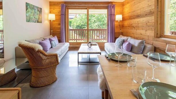 A cozy room with a sofa, a dining table set with wine glasses, and a view through large windows. - Fauvettes 4 a warm cocoon in Meribel Village (Les Allues)