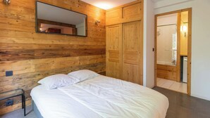 A bedroom with a wooden wall, a bed with white bedding, a nightstand, and a wooden wardrobe. - Fauvettes 4 a warm cocoon in Meribel Village (Les Allues)