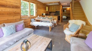 A wooden cabin interior with a dining area, sofa, and wicker chair. - Fauvettes 4 a warm cocoon in Meribel Village (Les Allues)