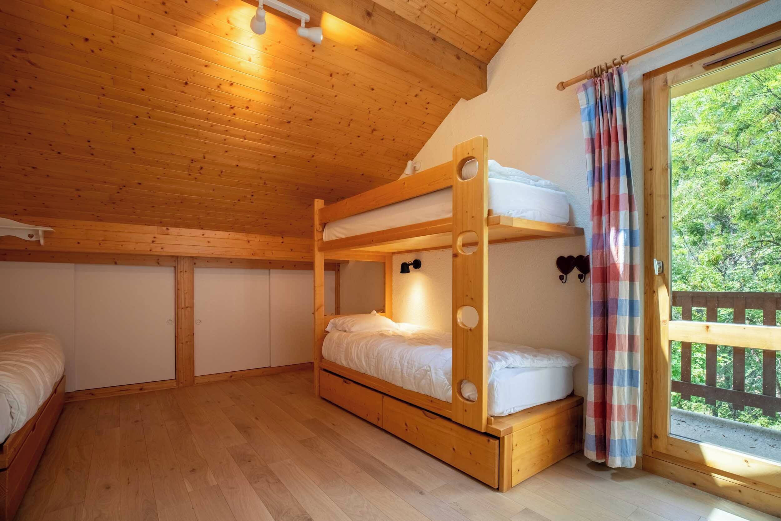A wooden bunk bed room with a window and curtains.