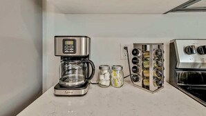 Una cocina con cafetera, frascos de condimentos y estufa.