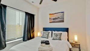 Una cama bien hecha con almohadas, una mesita de noche con lámpara y un cuadro en la pared.