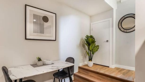 En matplats med ett bord i marmor, två svarta stolar, ett inramat konstverk, en krukväxt och en trappa som leder till en dörr.