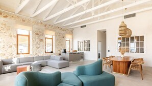 Amplia sala de estar con un sofá en forma de L, una mesa de comedor con sillas de madera y una cocina al fondo.
