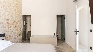 Un dormitorio con una cama grande, una bañera y una pared de piedra.