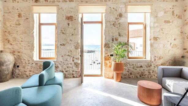 Una habitación amplia con pared de piedra, un ventanal y vista al mar.