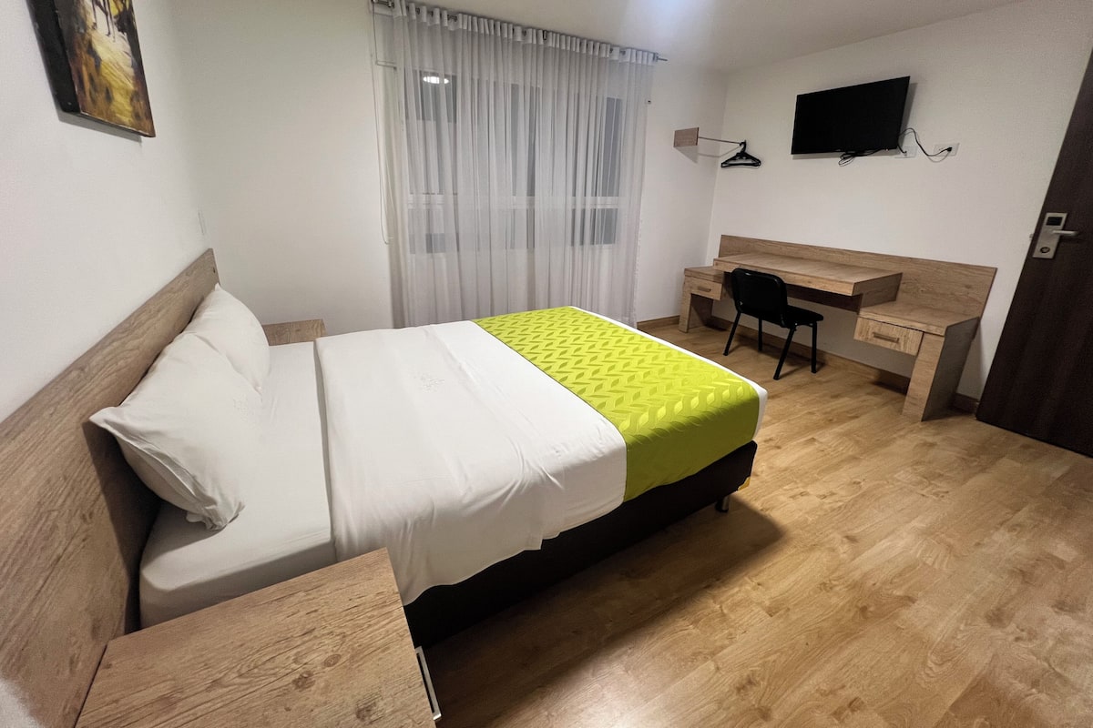 A hotel room with a bed, a desk, a chair, a TV, and a window with curtains.