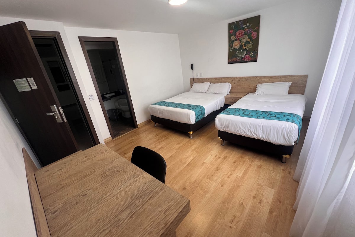 A hotel room with two beds, a wooden desk, and a painting on the wall.