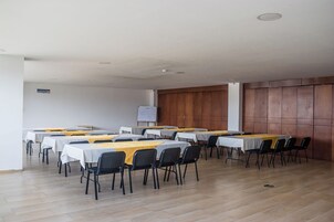 Uma sala de conferências com várias mesas e cadeiras, paredes brancas e lambris de madeira em uma das paredes.